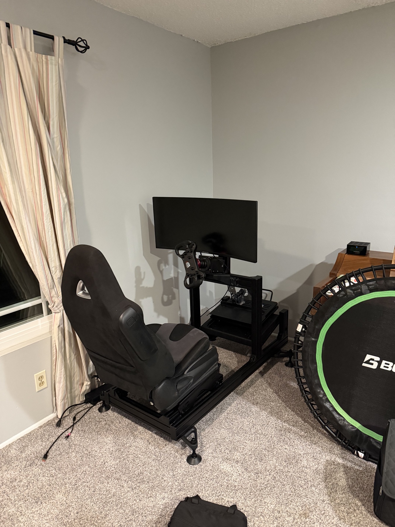 Single-screen sim racing cockpit with a seat, steering wheel, pedals, and monitor fitted into a room corner.